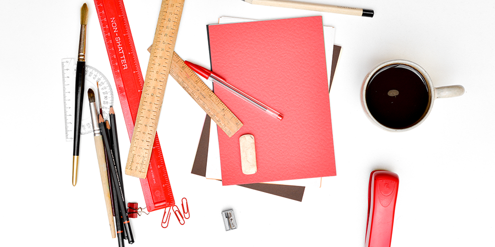 Collection of tools that might be used in design, such as pencils, pens, rulers, a notebook, and a mug full of coffee.