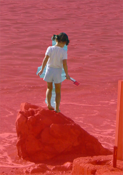 Image of a girl standing on a rock at the ocean, with a red overlay over most of the image. The girl and some of the ocean show up in their normal colors, indicating the selected area.