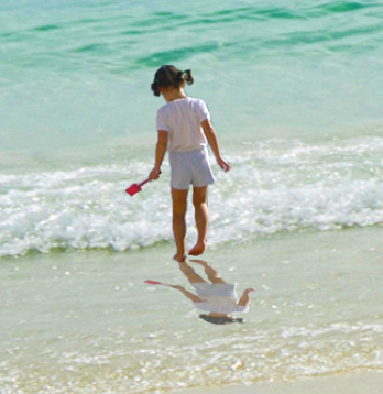 Close-up of the image of the girl on the beach, showing her standing in the water with an undisturbed, smooth reflection at her feet.