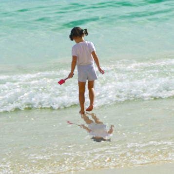 Close-up photo of the girl on the beach, with a reflection at her feet that looks more like it is part of the water.